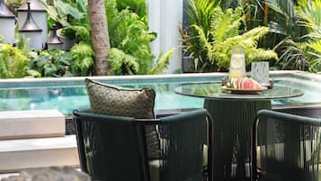 Un espace aménagé au bord de la piscine, avec une table en verre, des fauteuils en osier et une vue sur la piscine.