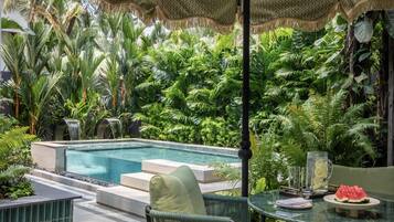 A pool area with a glass table, chairs, and a watermelon on the table.
