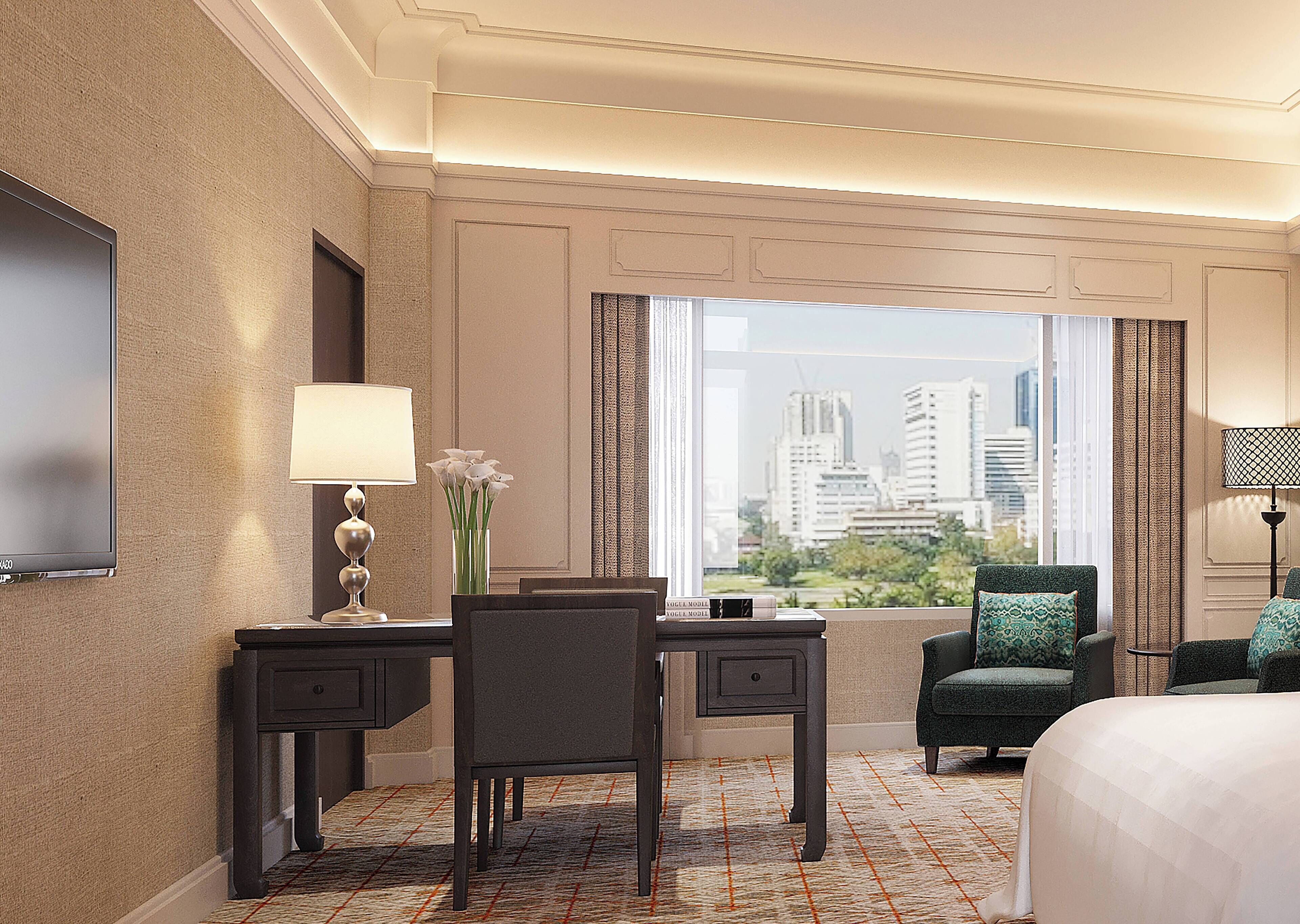 Een hotelkamer met een bed, een bureau met lamp, een stoel, uitzicht op een stadsbeeld door grote ramen en een flatscreen televisie aan de muur.