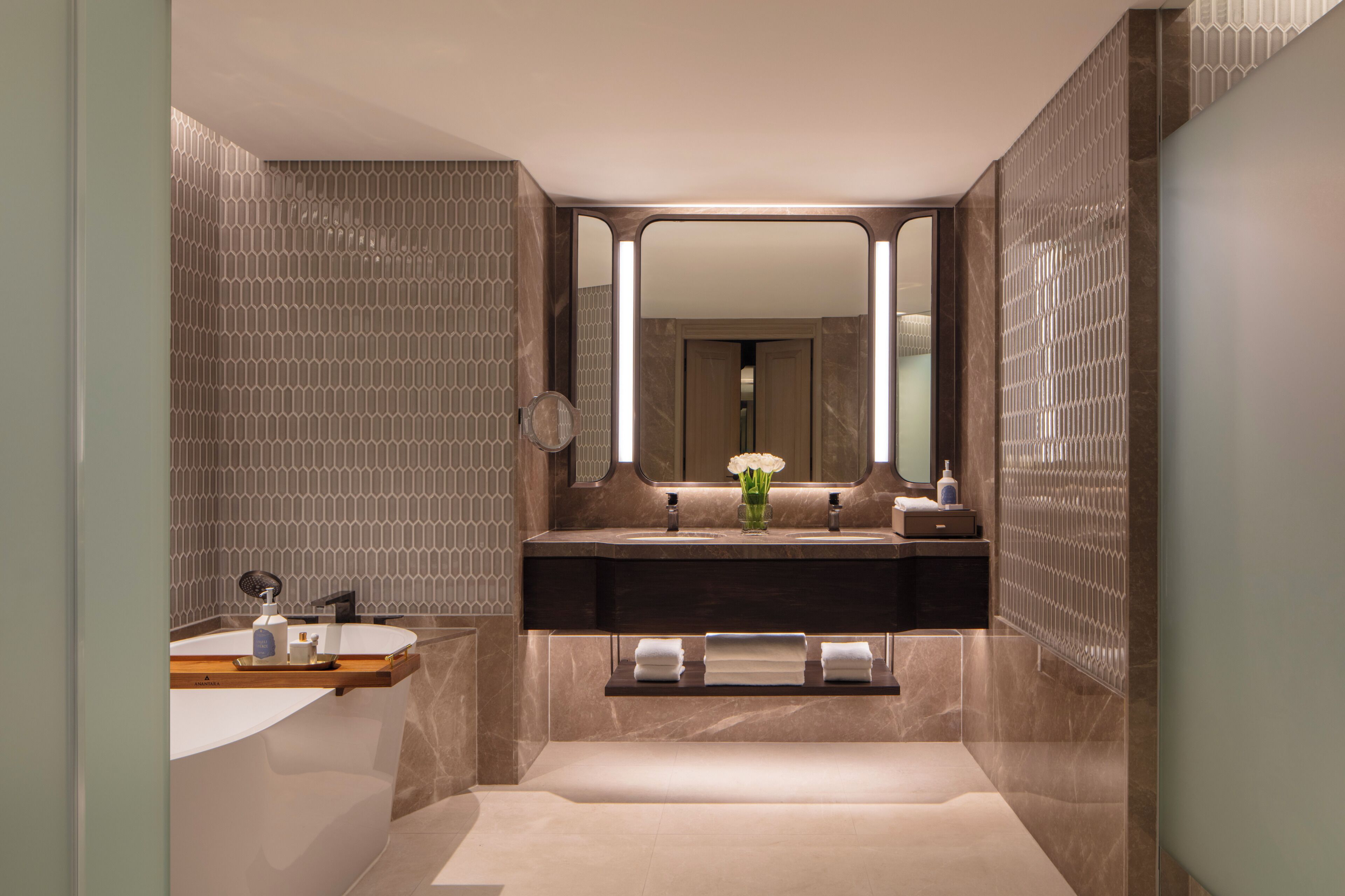 A modern bathroom with a large mirror, a bathtub, a vanity with a sink, and a towel rack.