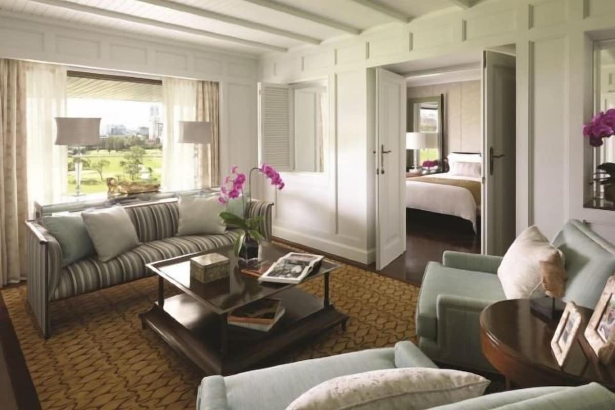 A hotel room with a sofa, armchair, and a bed with a nightstand.