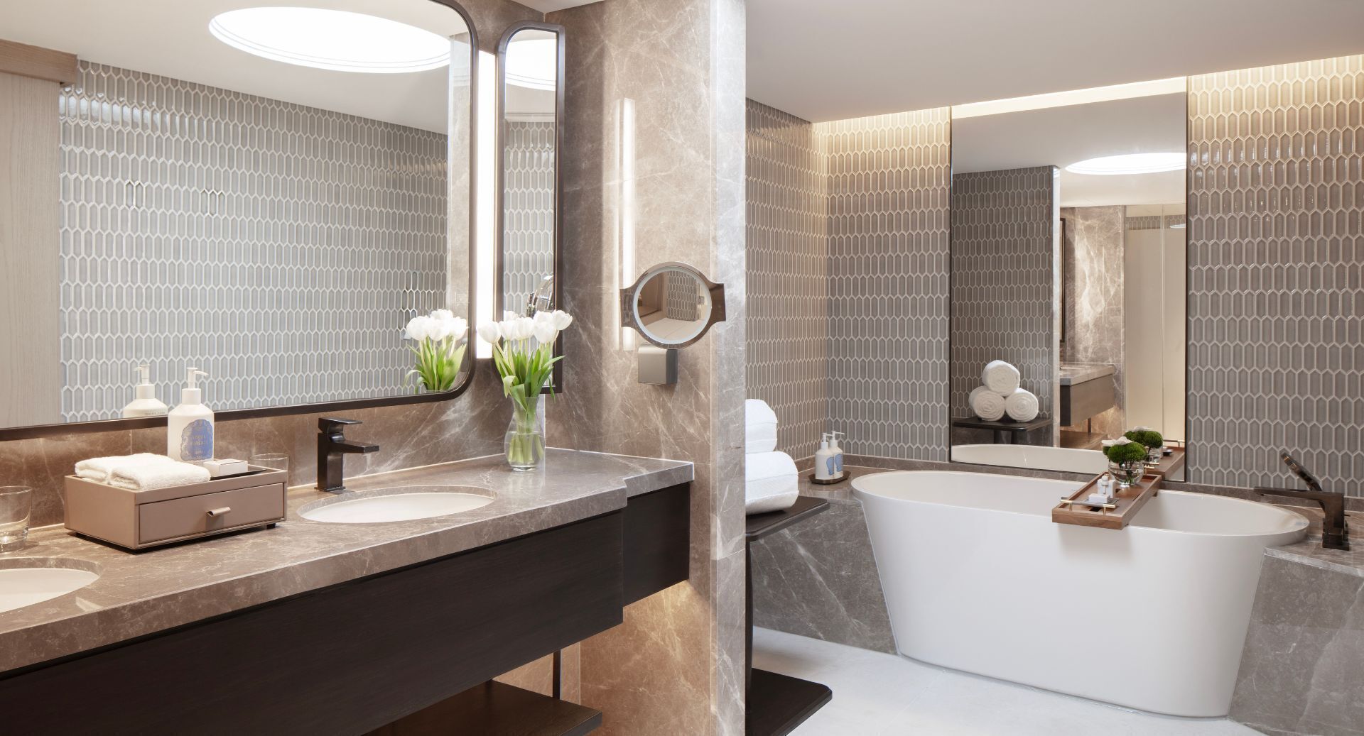 A modern bathroom with a large mirror, two sinks, a bathtub, and decorative elements like flowers and towels.
