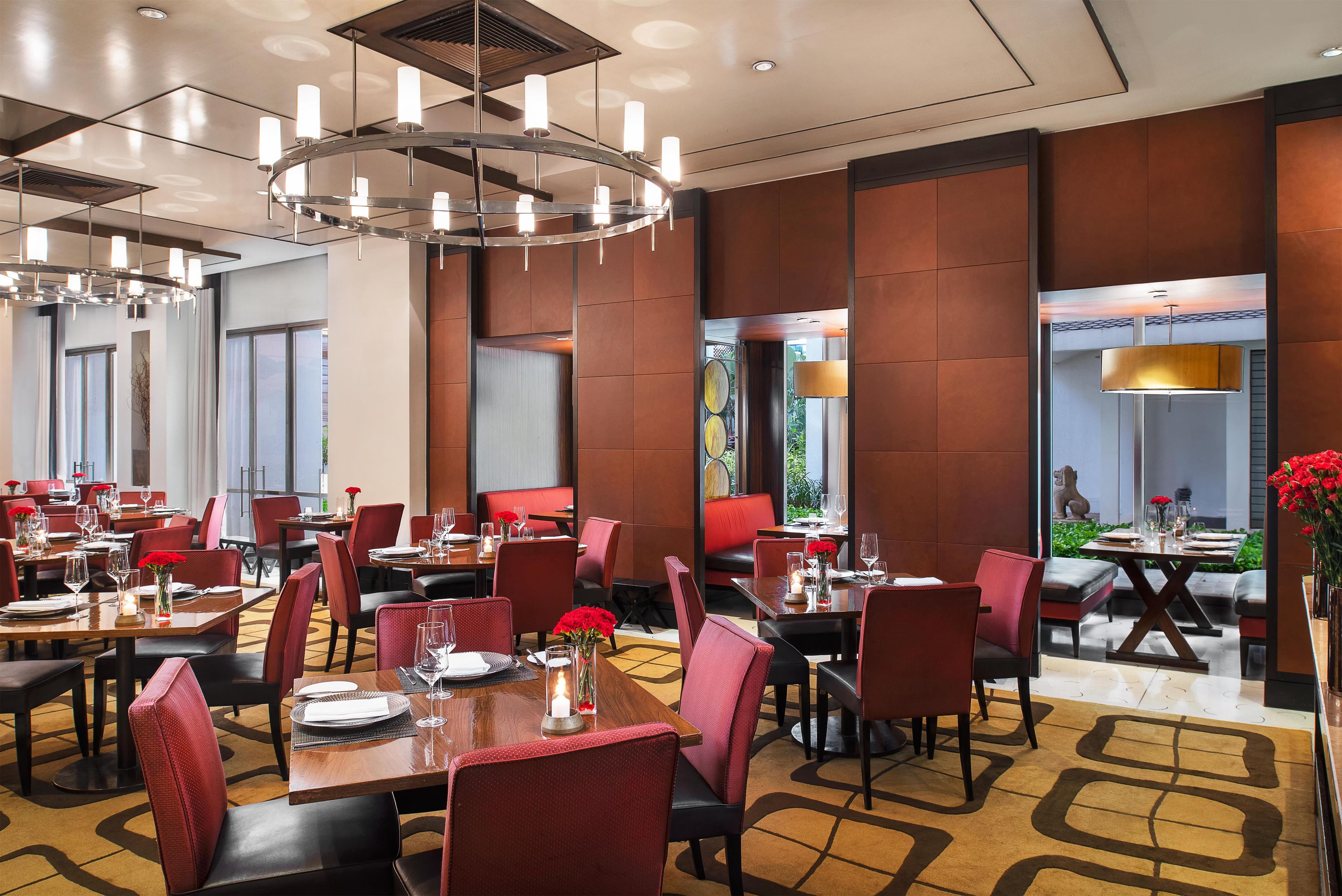 A modern dining area with multiple tables and chairs, a central chandelier, and large windows.