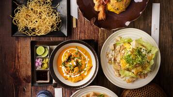 A variety of dishes on a wooden table, including noodles, soup, and a plate with a whole shrimp.