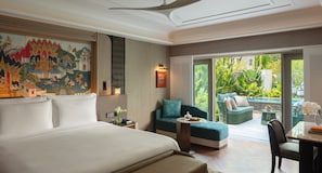 A hotel room with a large bed, a sofa, a dining table, and a view of a lush garden.