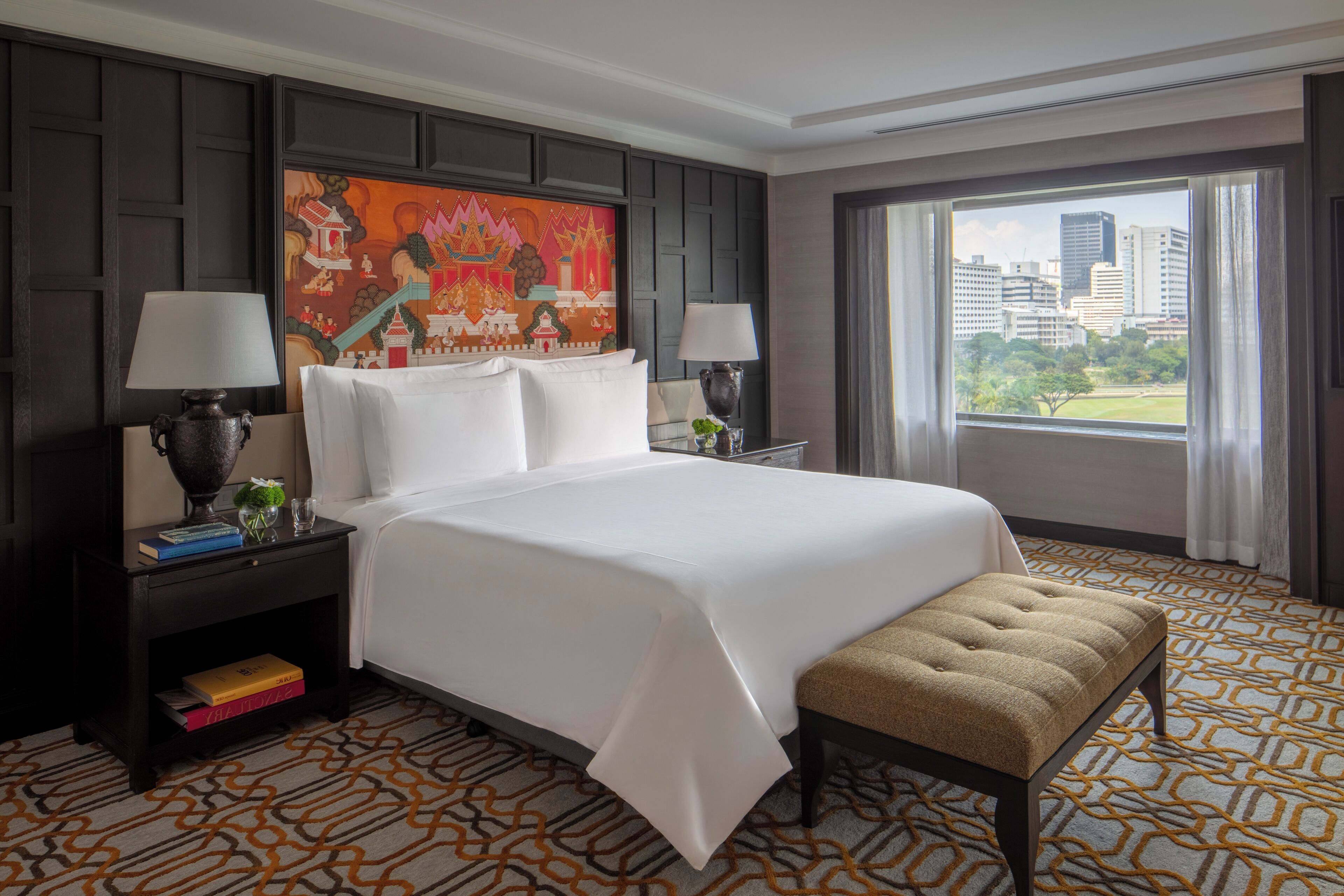A hotel room with a large bed, two bedside tables with lamps, a view of the city, and a patterned carpet.
