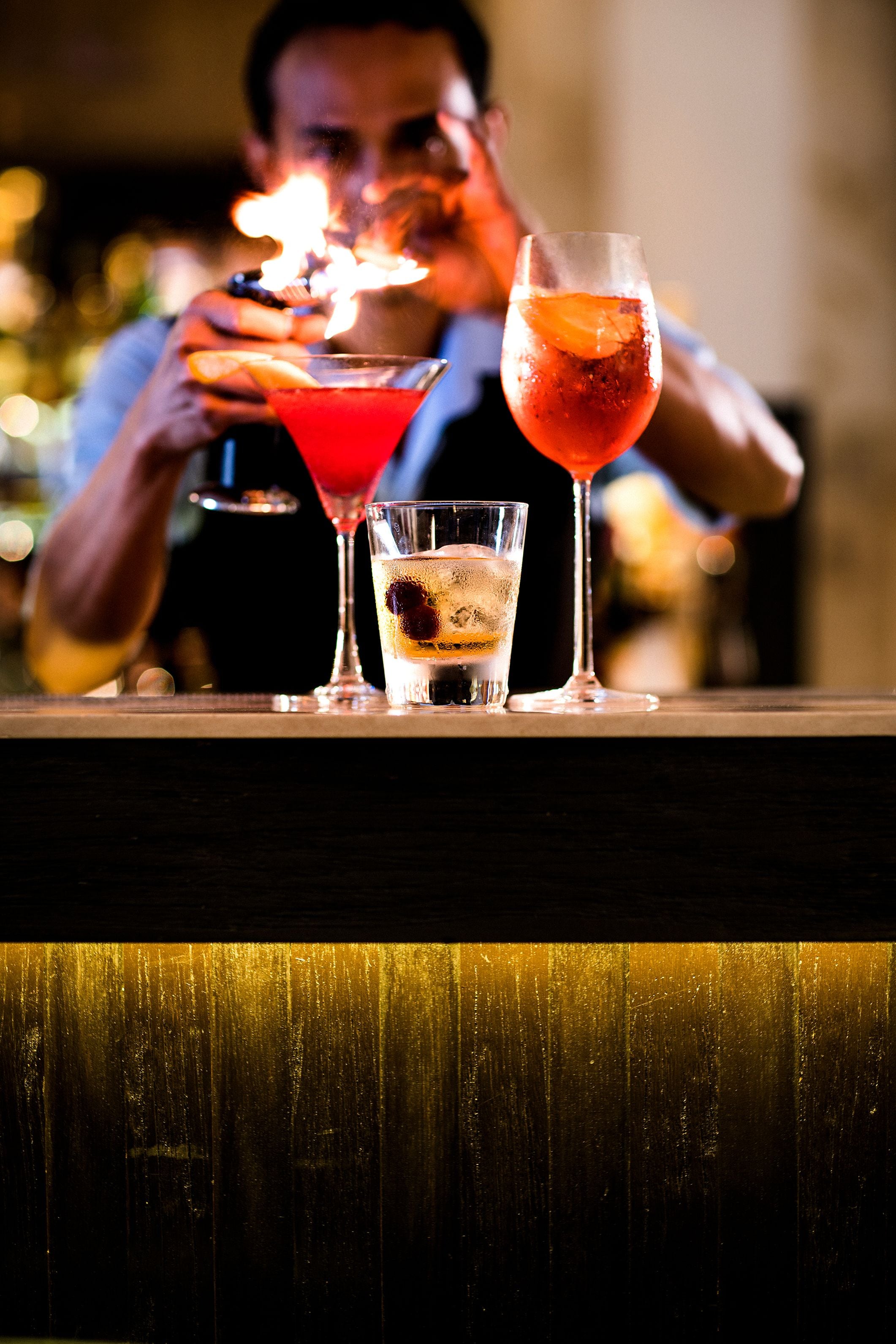 A bar with three cocktails, one with a flaming garnish.