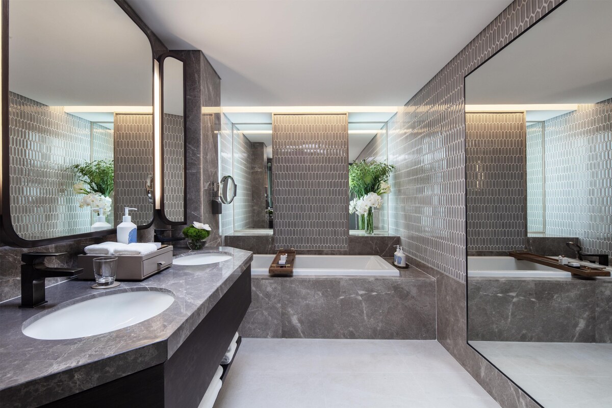 A modern bathroom with two sinks, a bathtub, and a large mirror.
