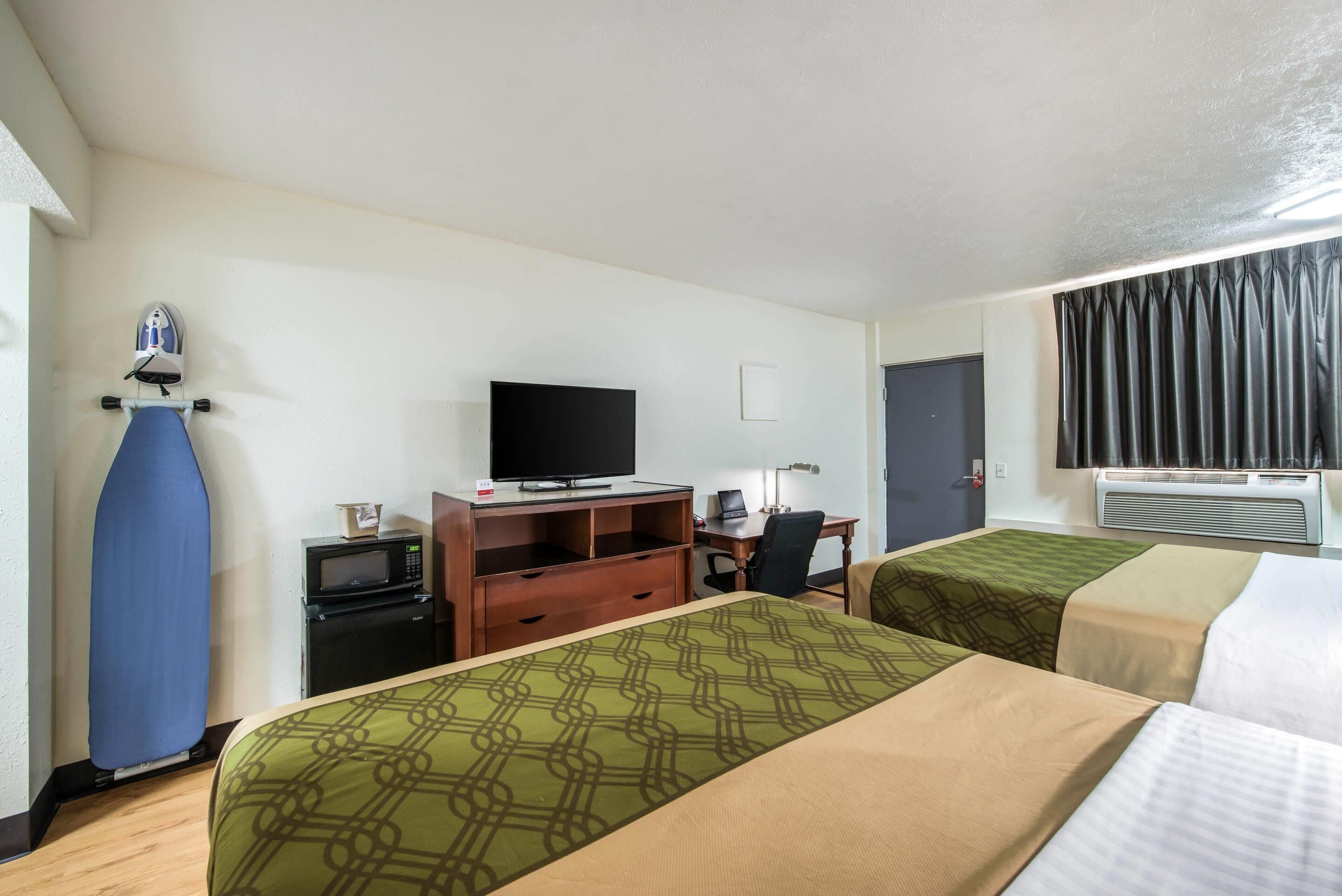 A hotel room with two beds, a TV, a desk with a computer, a microwave, and an ironing board.