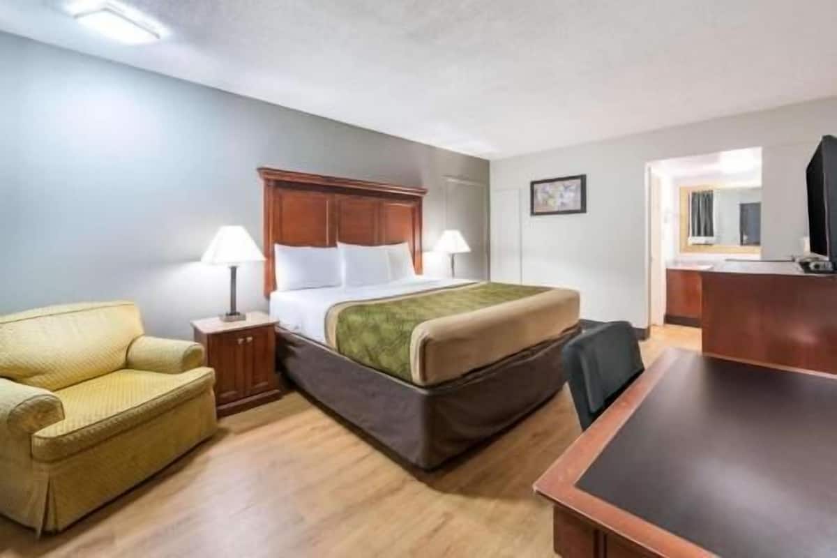Quarto de hotel com cama, escrivaninha, cadeira, luminária e uma mesinha.