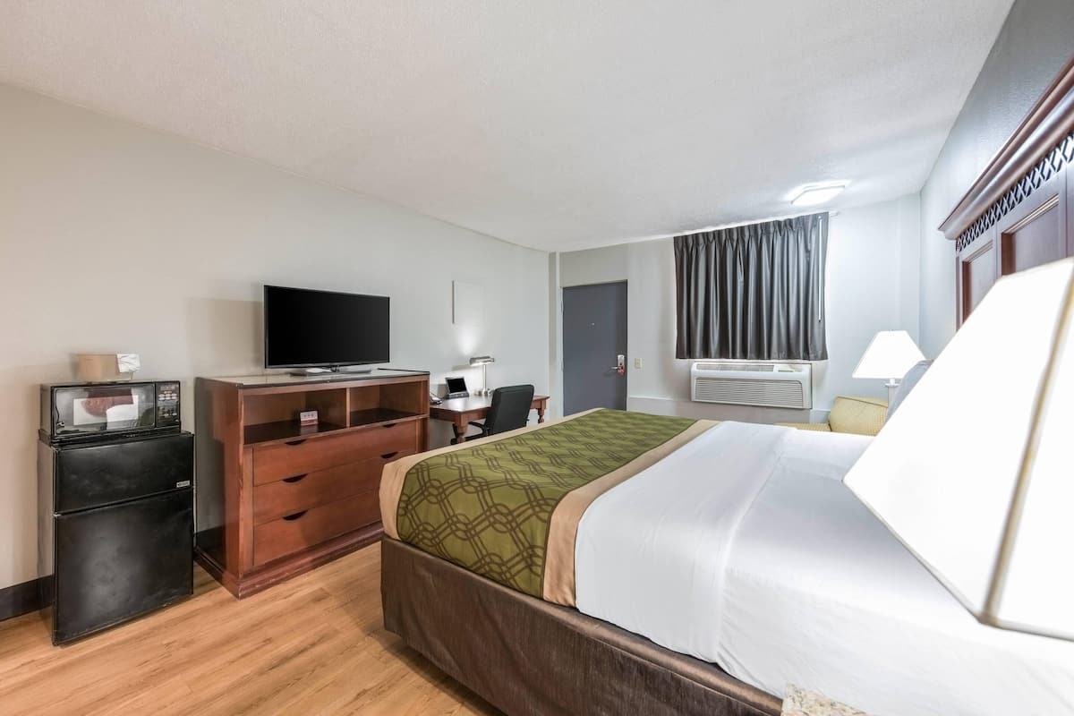 Quarto de hotel com cama, escrivaninha com computador, televisão, frigorífico e ar condicionado.