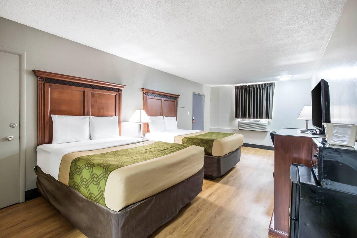 Quarto de hotel com duas camas, uma mesa, uma televisão e um ar condicionado.