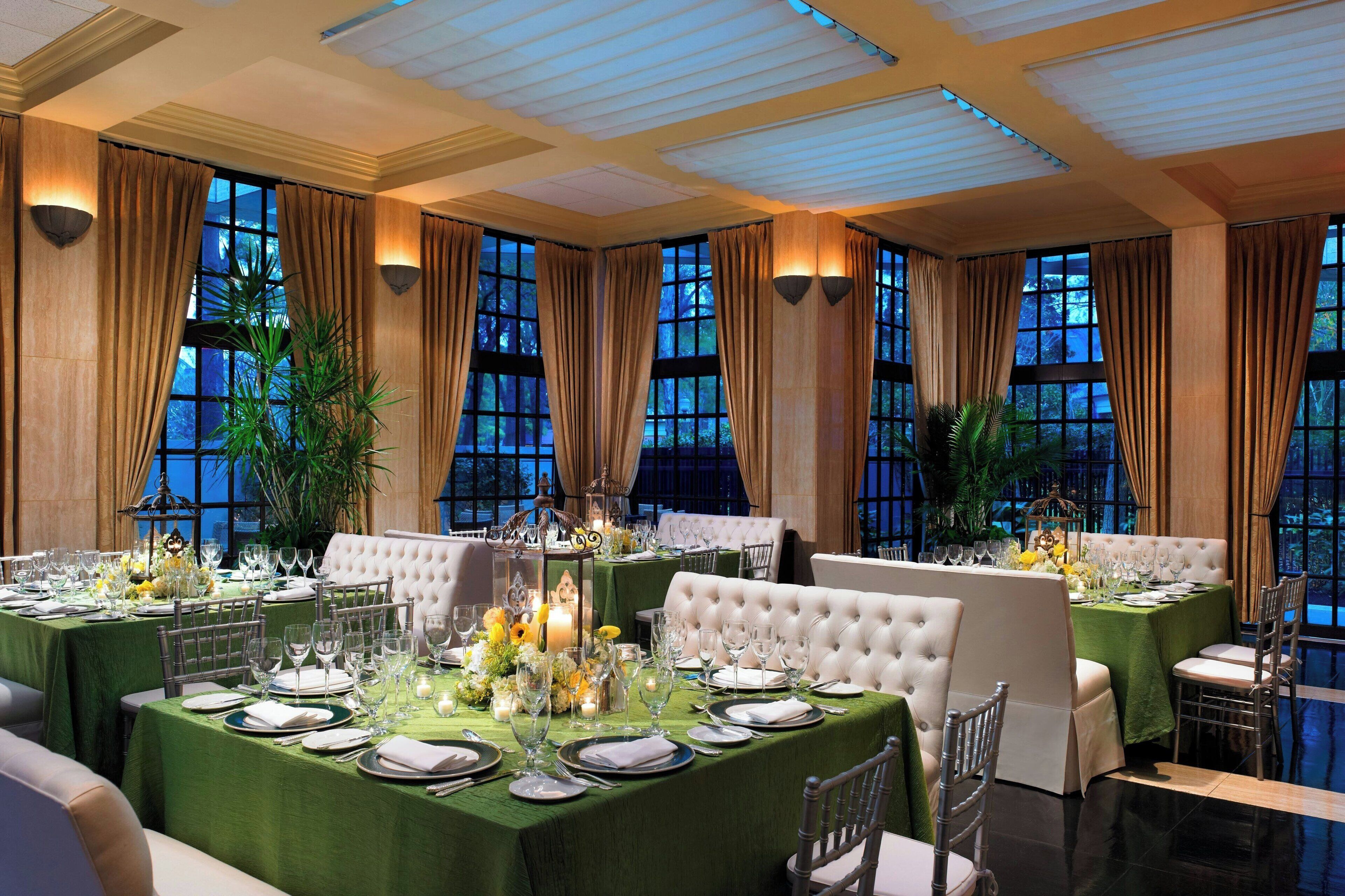 Une salle à manger élégante, avec plusieurs tables dressées pour un repas, de grandes fenêtres et un lustre.