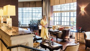 A spacious hotel lobby with a high ceiling, large windows, and a central seating area with a sofa and armchairs. - Houston Grand Hotel - River Oaks (Houston)