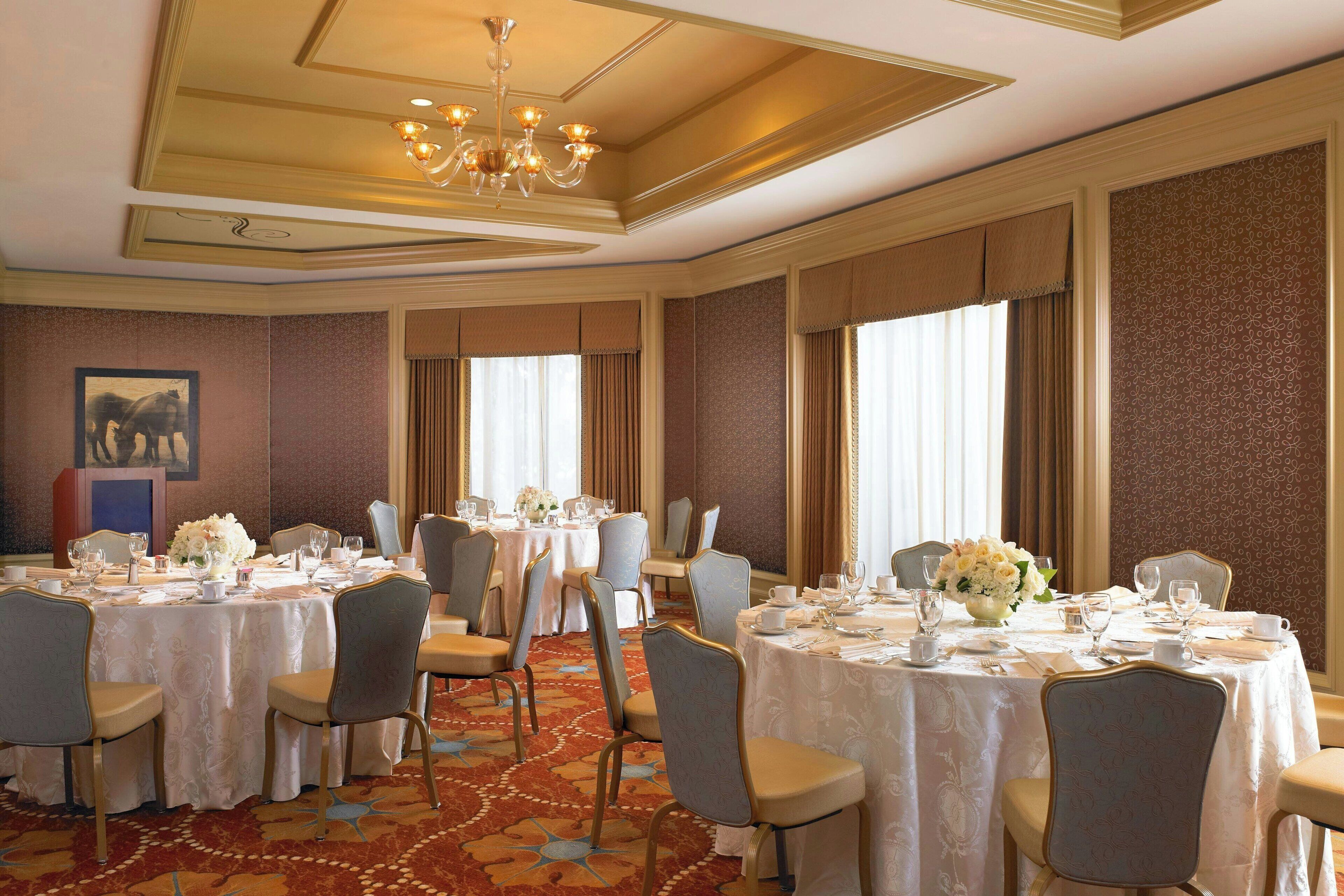 Une salle de banquet avec des tables rondes dressées pour le repas, agrémentée d’un lustre, d’un papier peint à motifs et d’un sol recouvert de moquette.