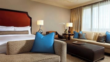 Una habitación de hotel con una cama, dos sofás, una mesita de centro y una mesita de noche con lámparas.