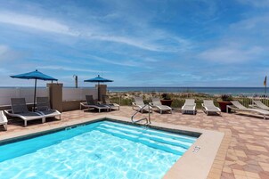 Une piscine sur le toit, agrémentée de chaises longues et de parasols, avec vue sur une plage.