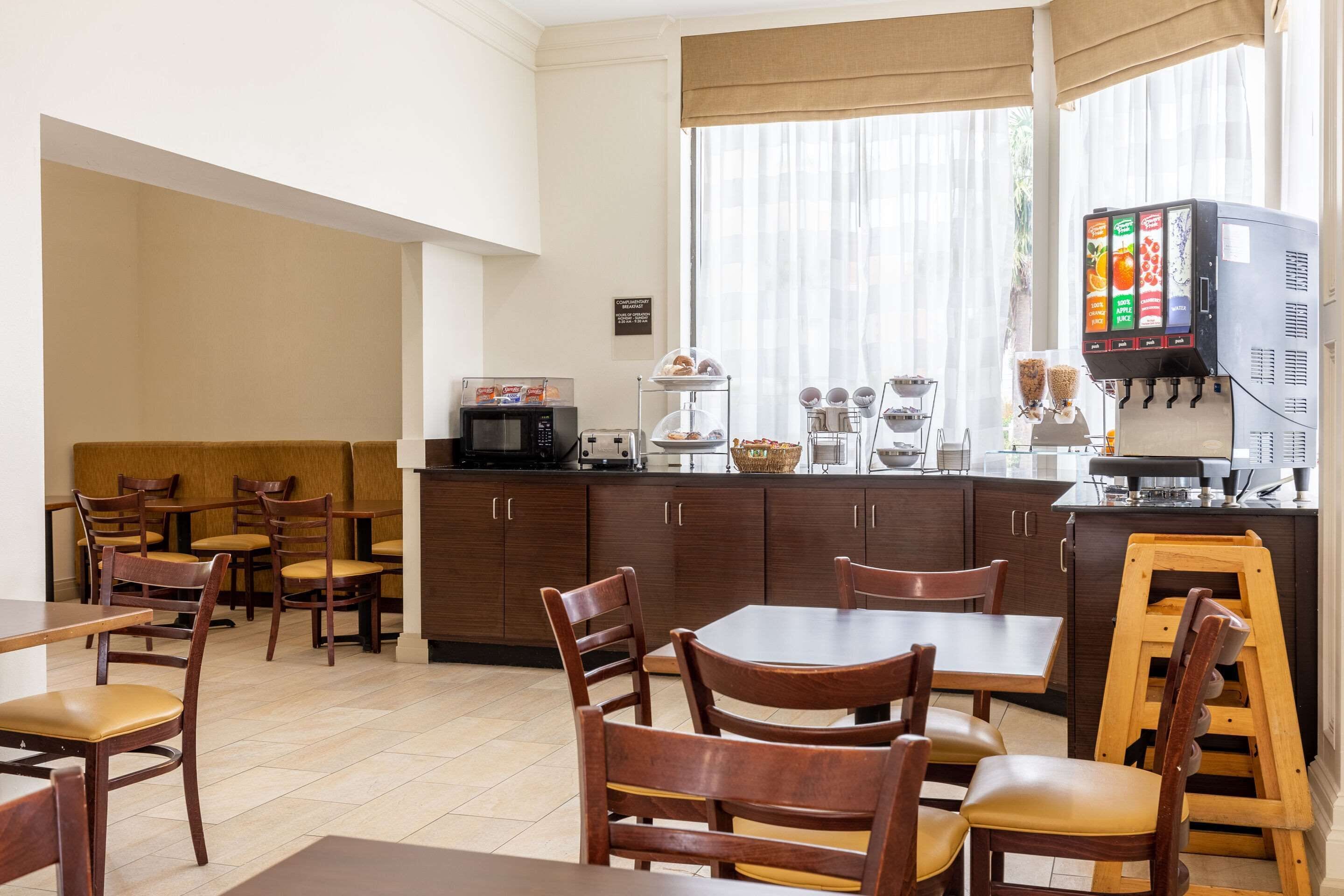 A hotel dining area with wooden tables and chairs, a buffet station, and a coffee machine.