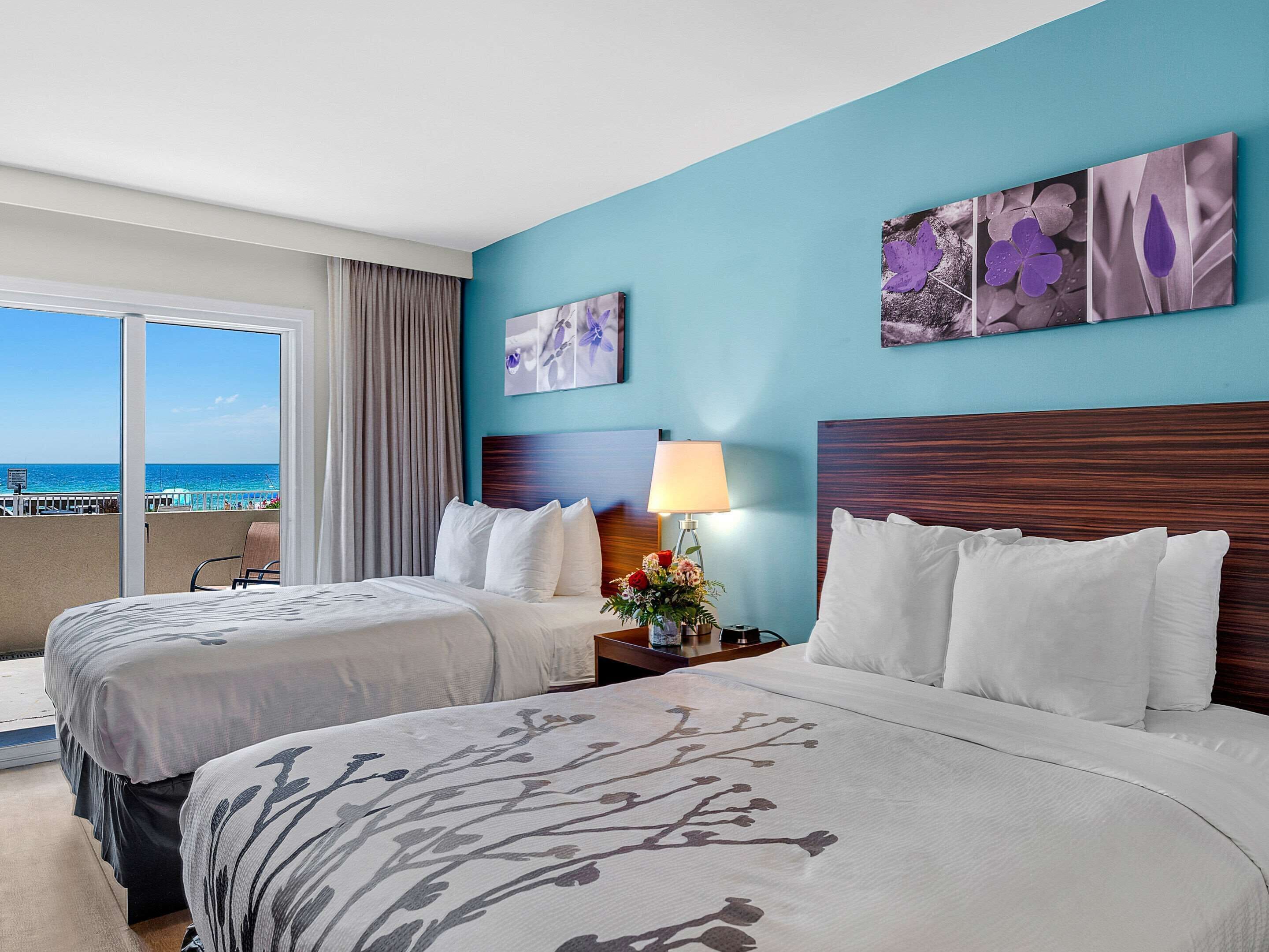 Habitación de hotel con dos camas, vista a la playa y obras de arte en las paredes.