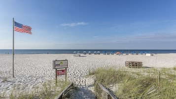 A sandy beach with an American flag, beach umbrellas, and a wooden structure.