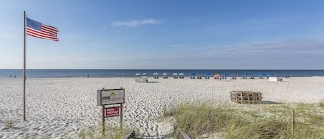 A sandy beach with an American flag, beach umbrellas, and a wooden structure.