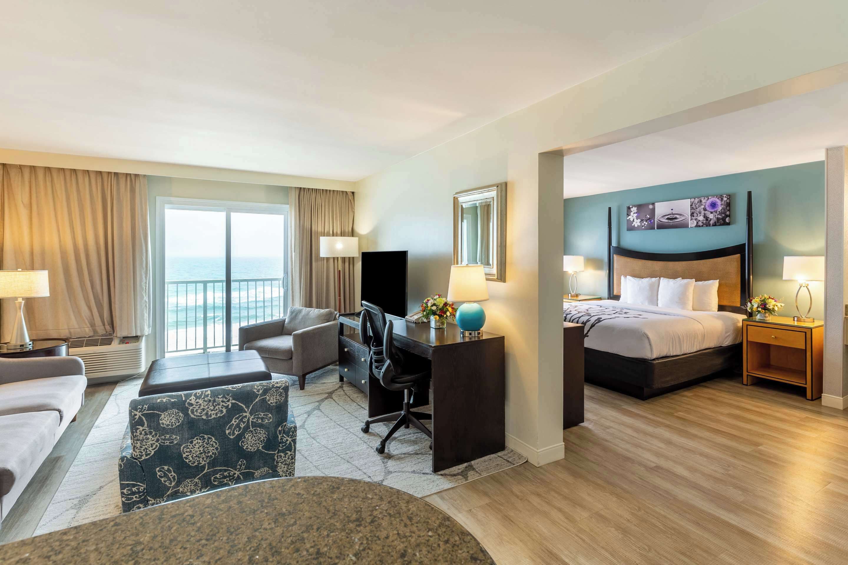 A hotel room with a bed, desk, chair, and a view of the ocean.