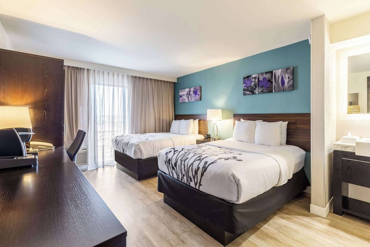 A hotel room with two beds, a desk, and a large window with curtains.