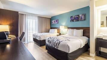 Habitación de hotel con dos camas, un escritorio y un ventanal con cortinas.