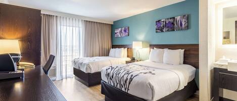 A hotel room with two beds, a desk, and a large window with curtains.