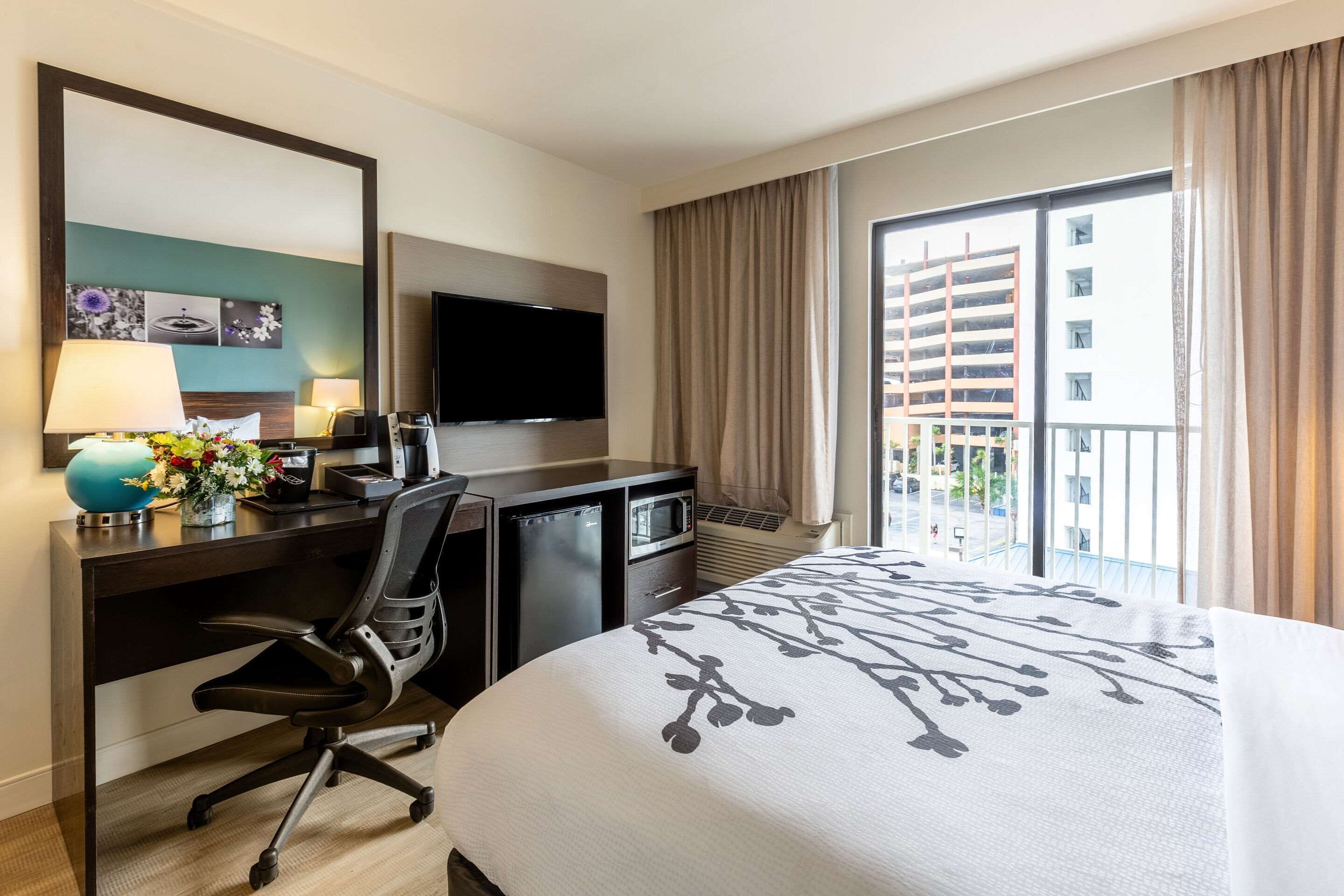 Una habitación de hotel con cama, escritorio, silla, televisor y ventana con cortinas.