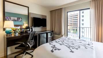 A hotel room with a bed, desk, chair, television, and a window with curtains.