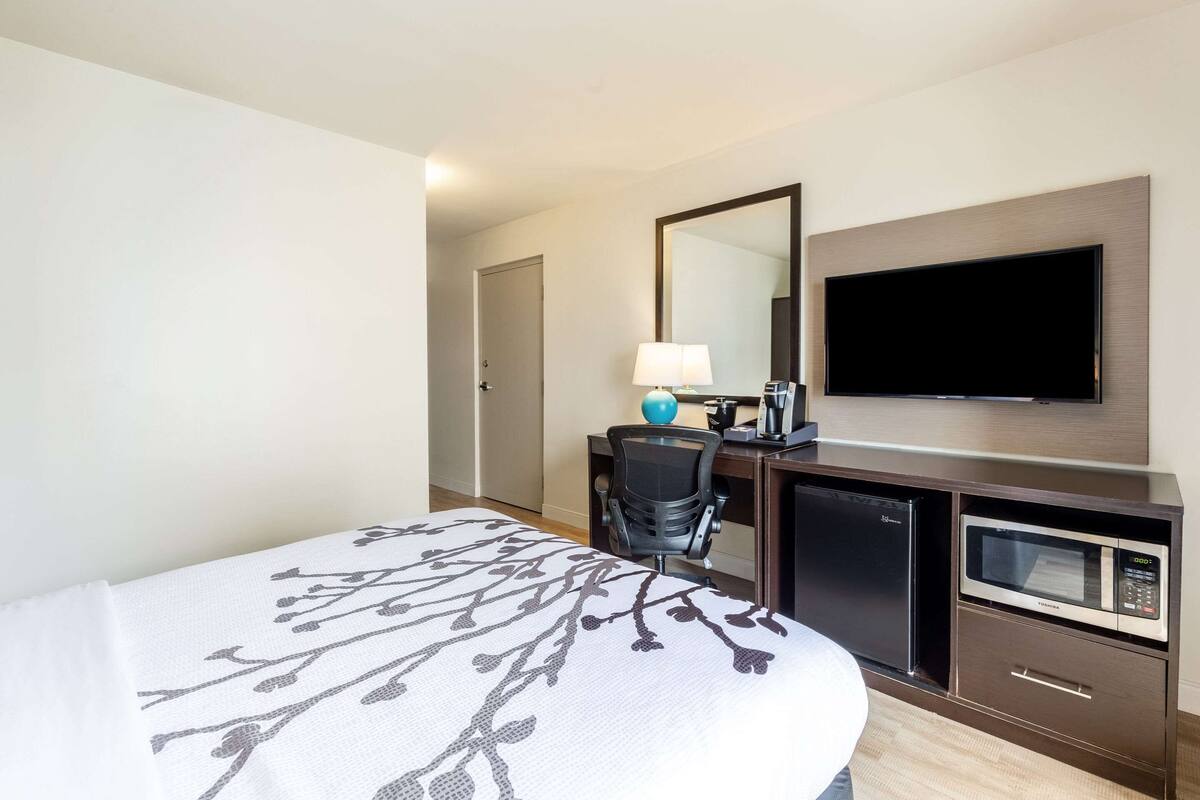 A hotel room with a bed, a desk with a computer, a microwave, and a TV.