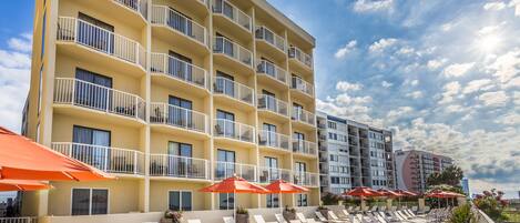 A hotel with multiple balconies, outdoor seating with umbrellas, and a clear sky.