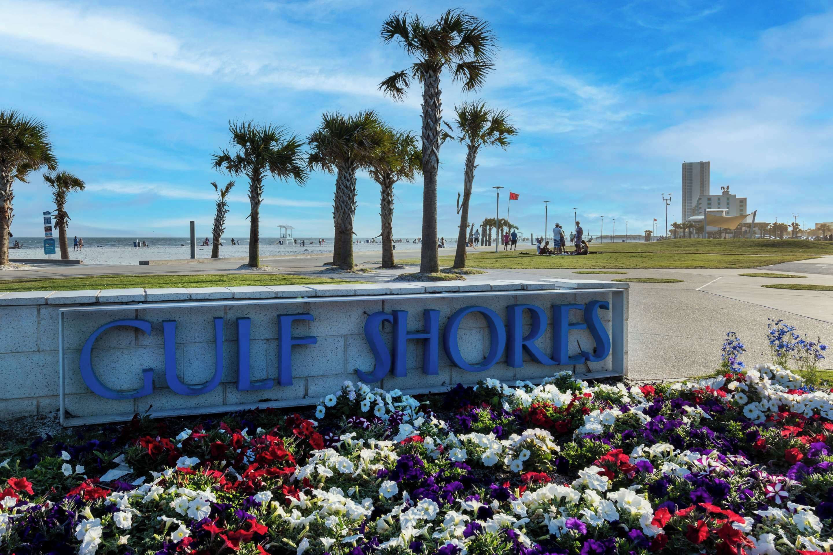 A sign reading "GULF SHORES" with a flower bed in front.