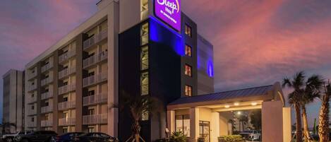 A Sleep Inn hotel with a prominent neon sign, multiple balconies, and a well-lit entrance.