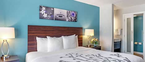 A hotel room with a large bed, two bedside tables with lamps, a nightstand with a vase, and a wall-mounted artwork.