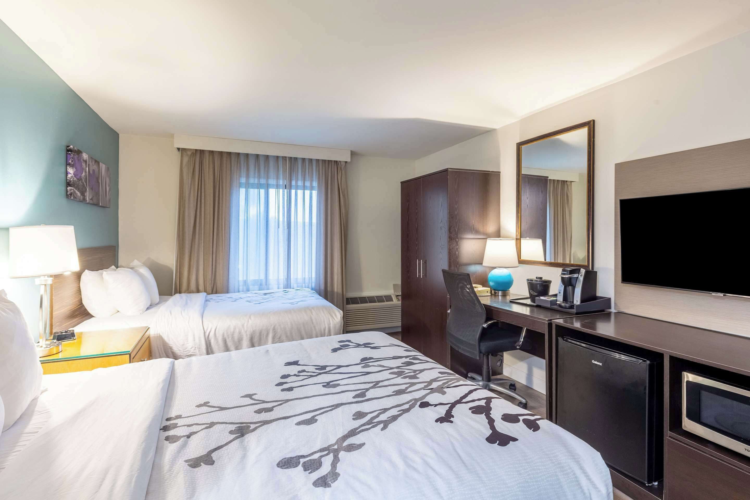 A hotel room with two beds, a desk with a computer, a TV, and a minibar.