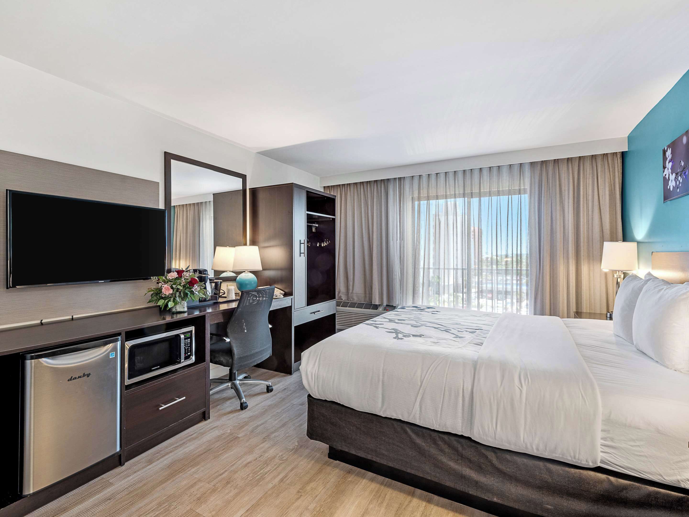 Een hotelkamer met een bed, een bureau met een computer, een televisie en een minibar.