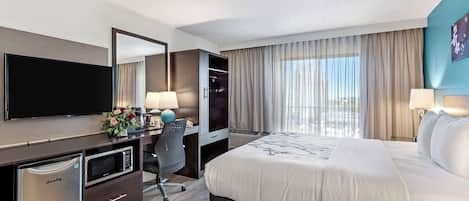 Een hotelkamer met een bed, een bureau met een computer, een televisie en een minibar.