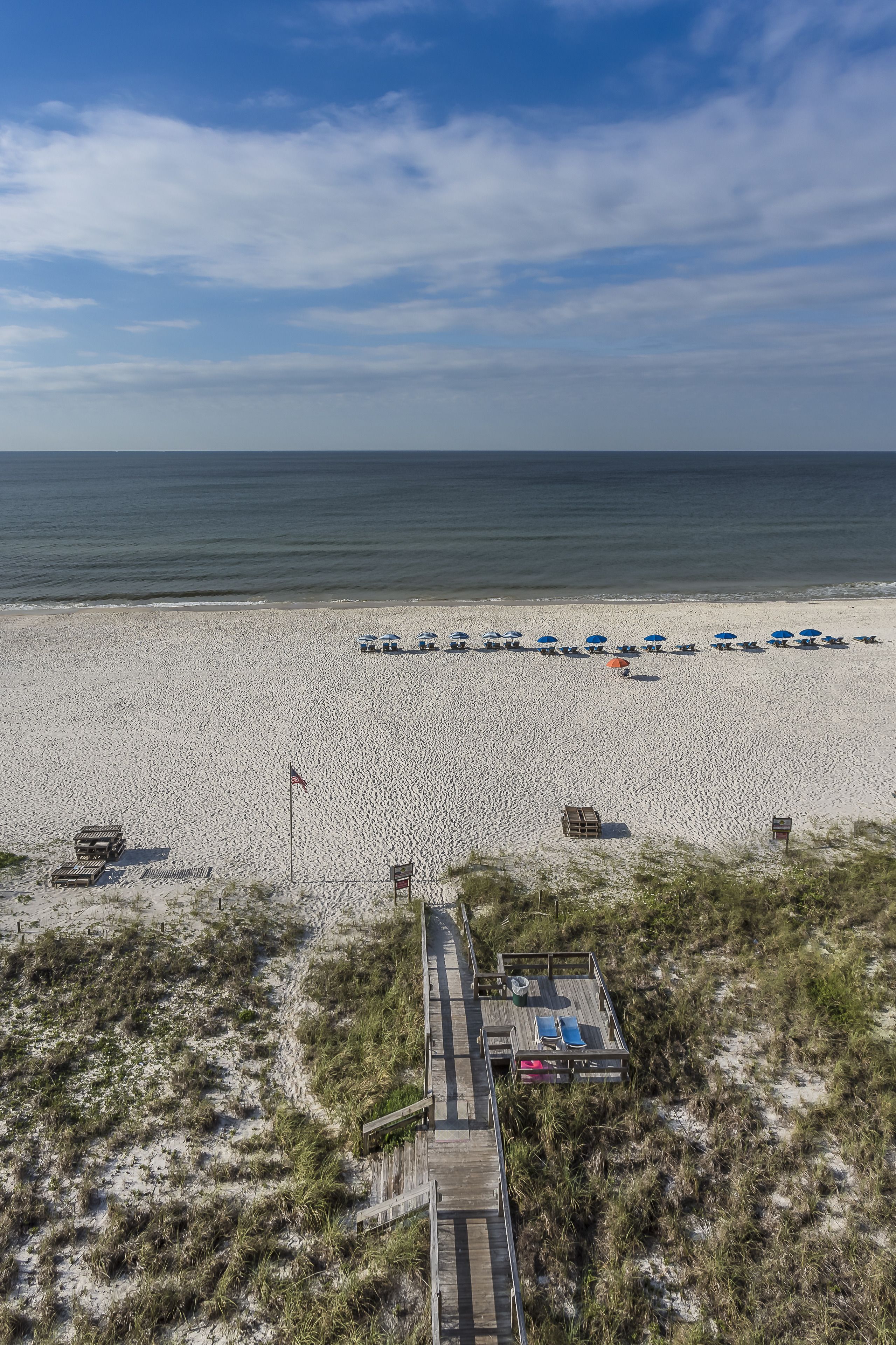 A beach with a wooden boardwalk leading to beach umbrellas and lounge chairs.
