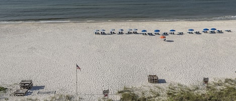 A beach with a wooden boardwalk leading to beach umbrellas and lounge chairs.