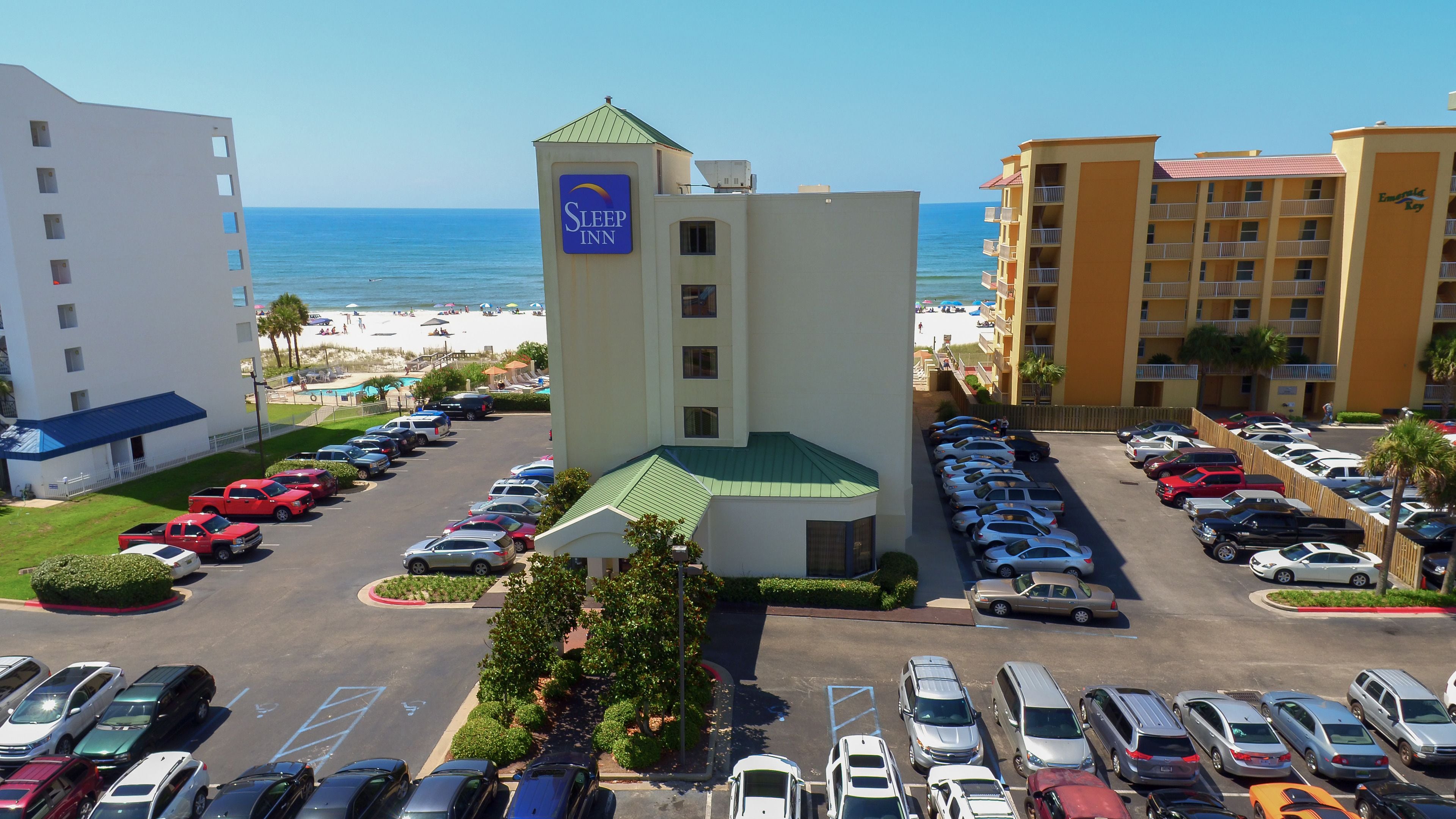 Een hotel met een zwembad, een parkeerplaats en uitzicht op het strand.