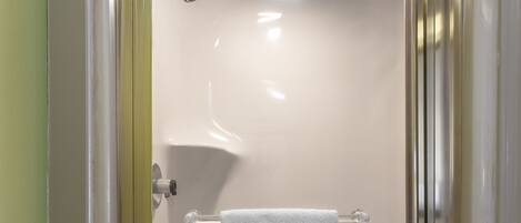A bathroom with a glass shower enclosure, a white towel hanging on a rack, and a visible showerhead.