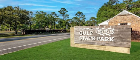 A wooden sign for Alabama's Gulf State Park with a road and greenery in the background.