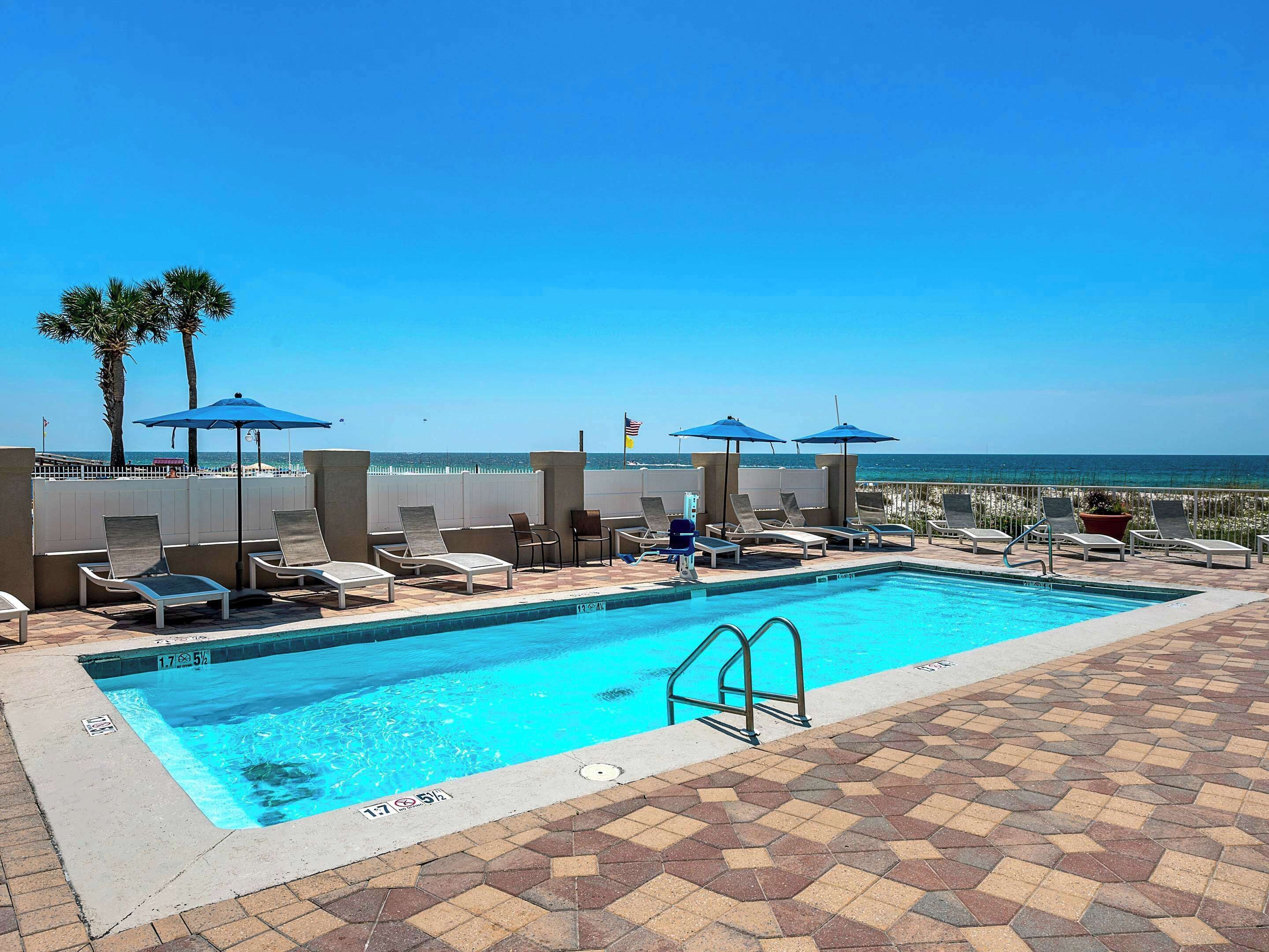 Ein Poolbereich mit Liegestühlen und Sonnenschirmen, mit freiem Blick auf das Meer und einer gefliesten Terrasse.