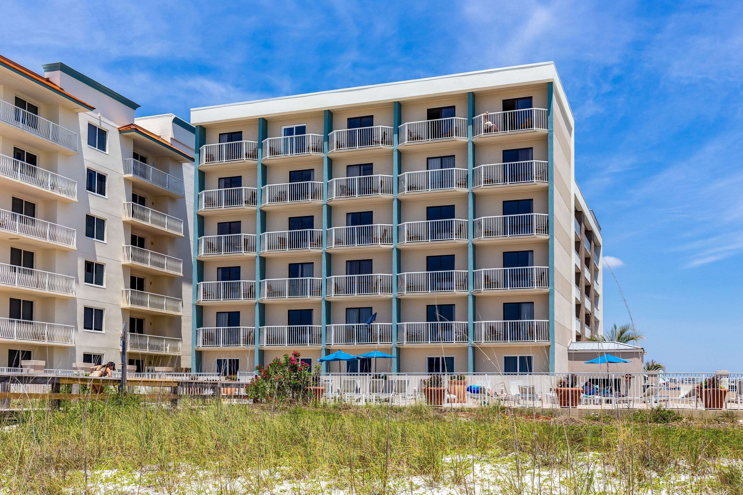 A multi-story hotel with balconies, outdoor seating, and a beach view.