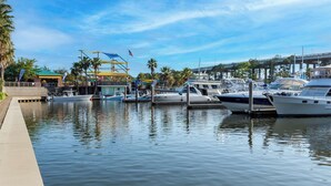 A marina with several boats docked, a bridge in the background, and a building with a green roof.