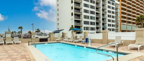 A swimming pool with lounge chairs and a tall building in the background.