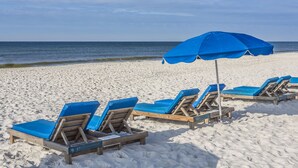 A beach with wooden lounge chairs and blue umbrellas.