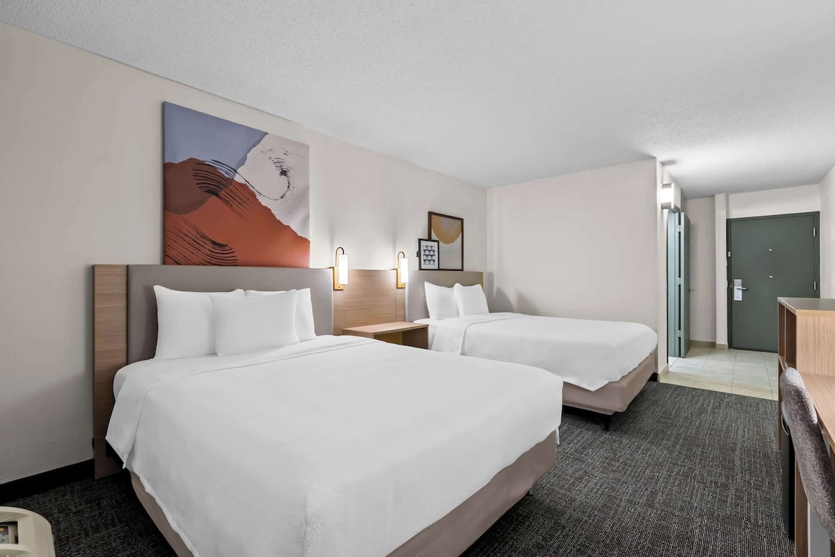 A hotel room with two beds, a painting on the wall, and a desk with a chair.